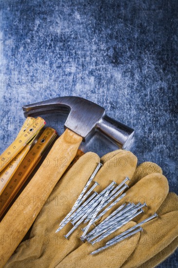 Leather safety working gloves set of construction nails wooden meter and claw hammer on scratched metallic surface building concept