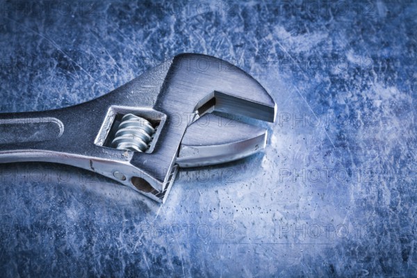 Stainless adjustable spanner on scratched metallic background top view image construction concept