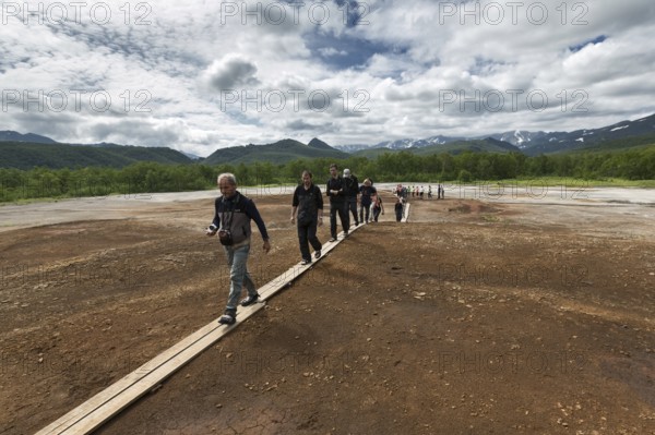 NALYCHEVO, KAMCHATKA, RUSSIA, JULY 30, 2014: Tourists walk on wooden deck, overlooking Thermal Pad Boiler, or Travertine Shield Boiler, with sleep and active griffins (mud pot) with thermal water