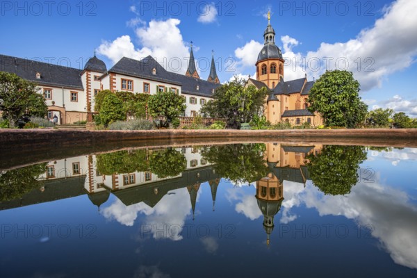 A historic monastery in the morning. Monastery walls, church and buildings are reflected in the water of a fountain. Beautiful garden in Seligenstadt Monastery, Germany, Europe