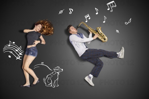 Happy valentines love story concept of a romantic couple against chalk drawings background. Male playing the saxophone for his girlfriend
