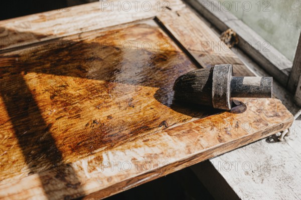 Varnished wooden surface under sunlight, highlighting texture with brush nearby