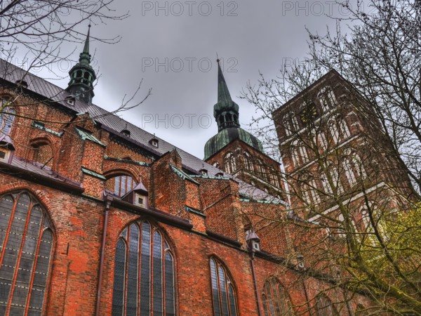 Gothic brick church with towers and large windows under a cloudy sky, surrounded by trees, stralsund, mecklenburg, germany