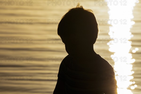 Silhouette of little boy by the sea at sunset