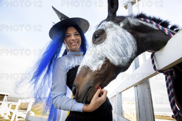 A girl dressed as a witch stands next to a horse on which a skeleton is drawn for the celebration of Halloween