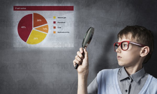 Cute boy looking through magnifying glass against graphs at chalkboard