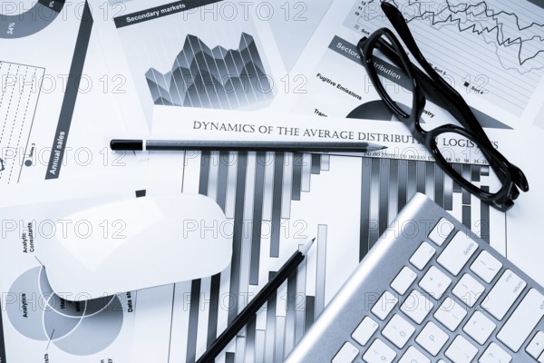 Business workplace with keyboard glasses and financial documents on table
