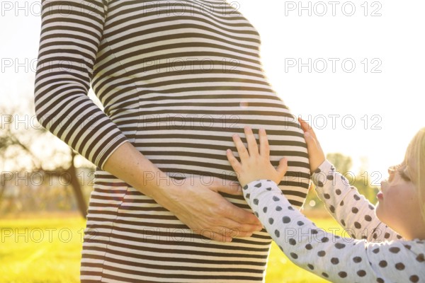 Young child touching the pregnant belly of her mother in beautiful evening sunlight