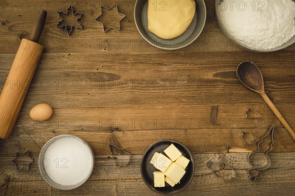 Collection of ingredients and utensils for baking Christmas biscuits with text space in the centre of the picture on a dark wooden background