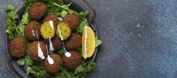 Plate of fried falafel balls served with fresh green cilantro and lemon top view on rustic concrete background. Traditional vegan dish of Middle Eastern cuisine, space for text, food photography, food photography