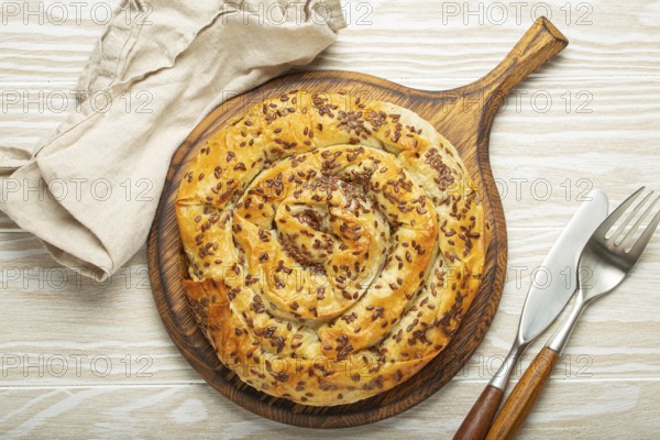 Burek made of filo dough with filling on cutting board, white wooden rustic background top view. Traditional savoury spiral pie of Balkans, Middle East and Central Asia, food photography, food photography