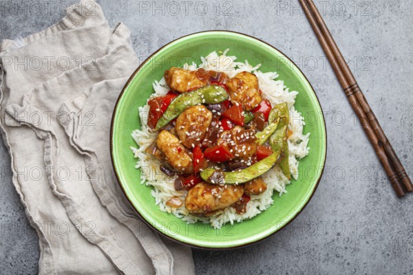 Asian sweet and sour sticky chicken with vegetables stir-fry and rice in ceramic bowl with chopsticks top view on gray rustic stone background, traditional Asian dish, food photography, food photography