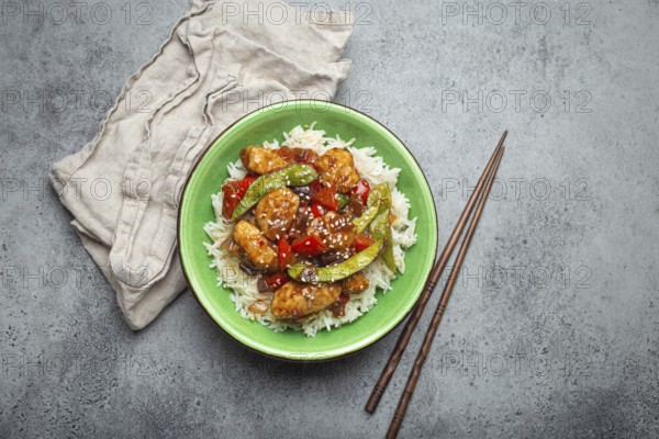 Asian sweet and sour sticky chicken with vegetables stir-fry and rice in ceramic bowl with chopsticks top view on gray rustic stone background, traditional Asian dish, food photography, food photography