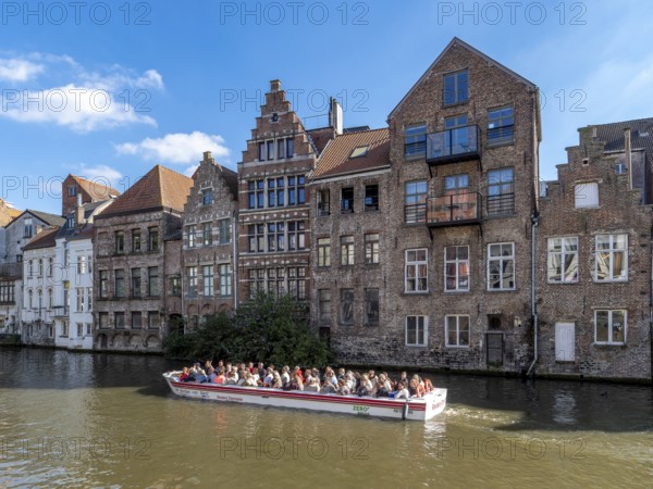 Tourists in the tourist boat for the canal cruise on the river Leie and in the background together indebted medieval historic buildings in the medieval city centre, Ghent, East Flanders, Belgium, Europe