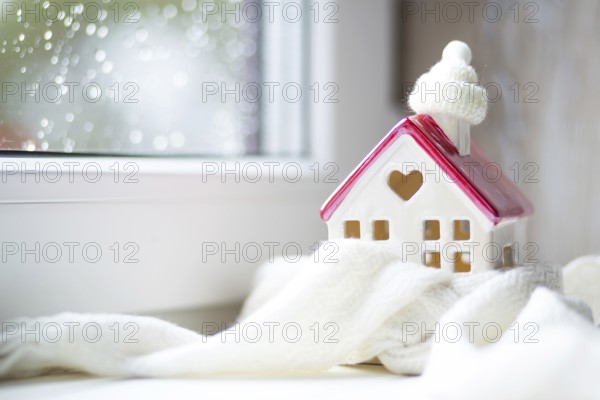 Cozy house is wrapped in a hat and scarf in a snowstorm -window sill decor. Winter, snow, home insulation, protection from cold and bad weather, room heating system. Festive mood, Christmas, New Year