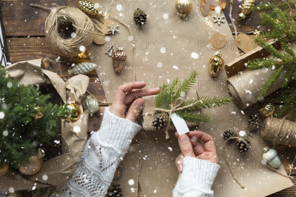 Hands pack a gift for Christmas and new year in eco-friendly materials: kraft paper, live fir branches, cones, twine, tied with a bow. Tags with mock up, natural decor, hand made, flatly. Festive mood