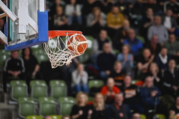Ball falls in the basket during basketball match. Audience in the background.