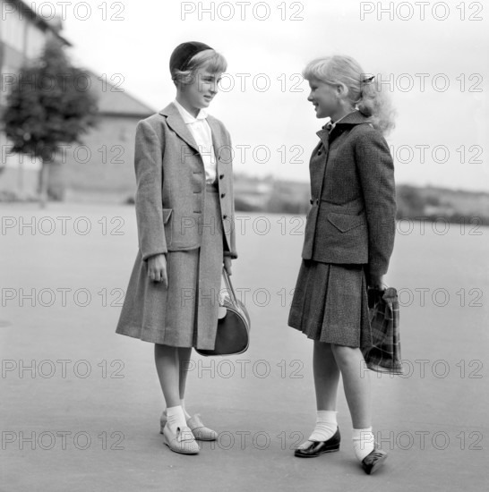Girls in the 1950s. Two teenage girls dressed in outfits typical of the decade. Typical schoolgirls holding their schoolbags standing outside the school building on the schoolyard. 1954. Conard ref 2722