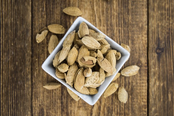 Roasted Almonds (in shell) on an old wooden table (close-up shot, selective focus)