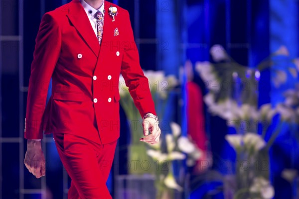 Male model walks the runway in red suit during a Fashion Show. Fashion catwalk event showing new collection of clothes. Single model