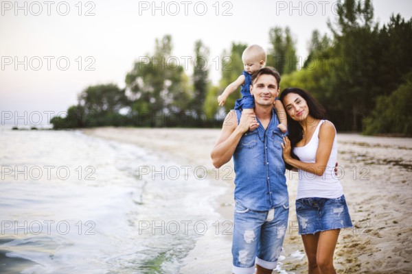 Beautiful young family on holiday with baby. The father holds the blonde girl in her arms, and the brunette's mother hugs her husband. The concept of a family beach holiday summer near the sea