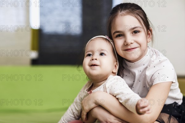 Elder sister with her little baby sister hugging in the bedroom. Siblings love