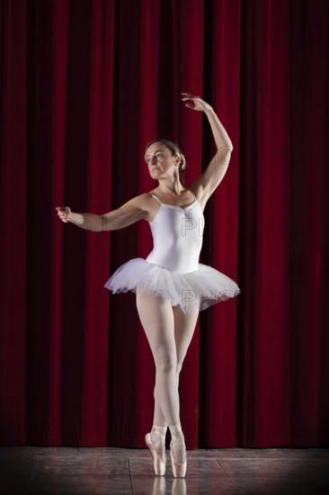 Ballet dancer in white ballet tutu in front of a red stage curtain in elegant pose, Mindelheim City Theatre, Mindelheim, Bavaria, Germany, Europe