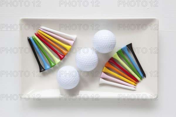 White ceramic dishes with golf balls and wooden tees on over white background, rectangle dish