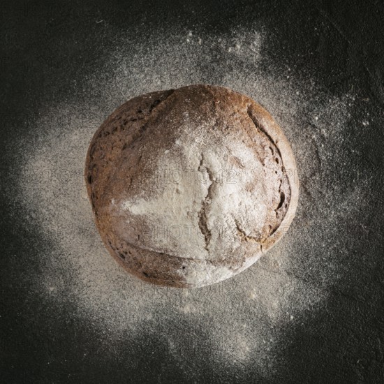 Whole homemade rye bread with rye flour on black textured background. Top view or flat-lay. Low key