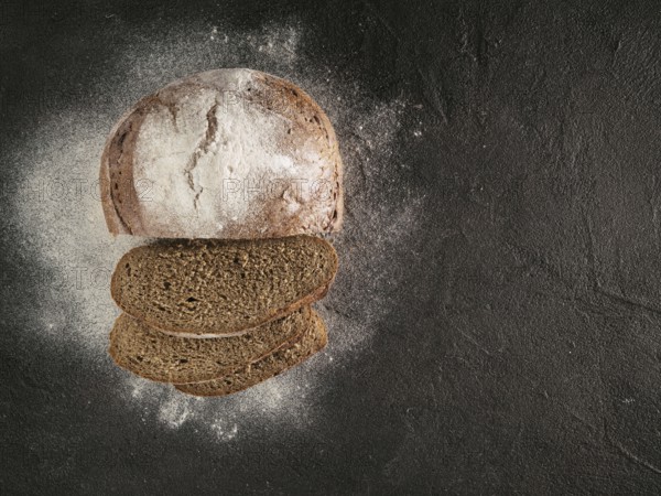 Sliced homemade sourdough rye bread with rye flour on black textured background. Top view or flat-lay. Copy space. Low key