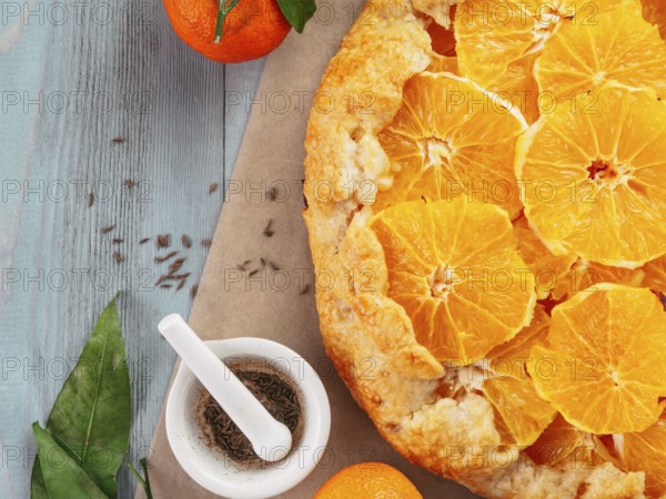 Top view of caraway and orange tart on baking paper over gray wooden table with copy space.Winter season and christmas ideas recipe-tart with caraway pastry and oranges, mandarines or tangerines
