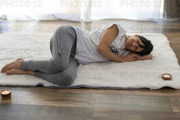 Yoga-clad woman smiling warmly at the camera while lying on a plush white rug