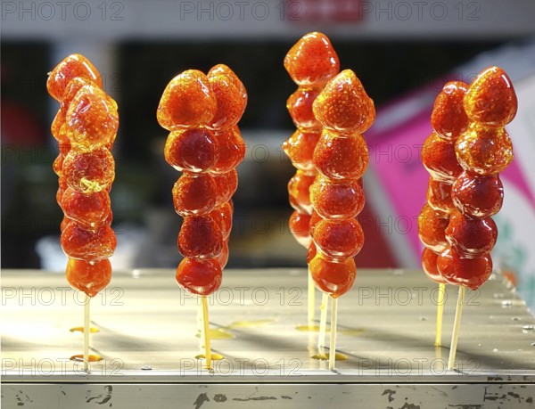 Strawberries glazed with sugar on skewers are sold at the market