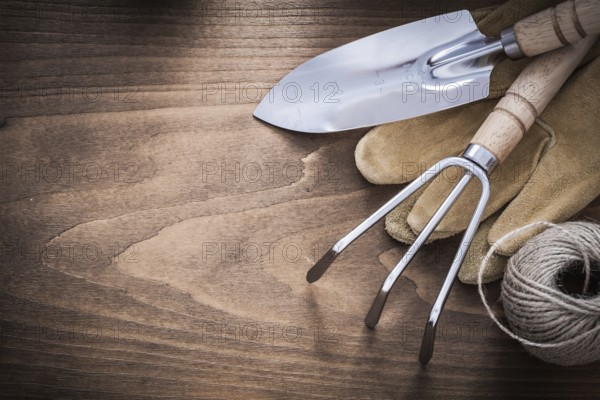 Metal hand spade rake brown leather gardening gloves and hank of string on vintage wood board agriculture concept