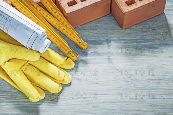 Composition of red bricks protective gloves blueprints wooden meter on wood board construction concept
