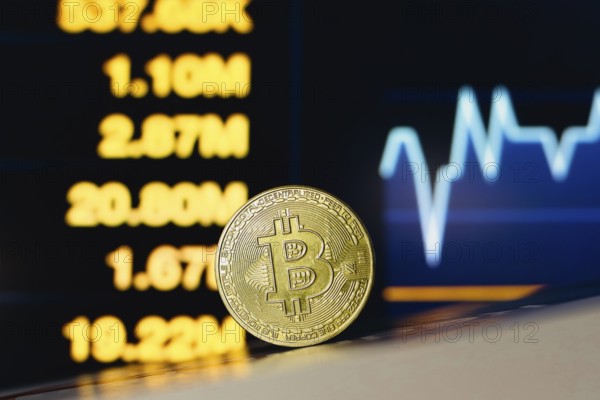 In this photo illustration, a Bitcoin coin is seen on the table and in the background, a stock market graph