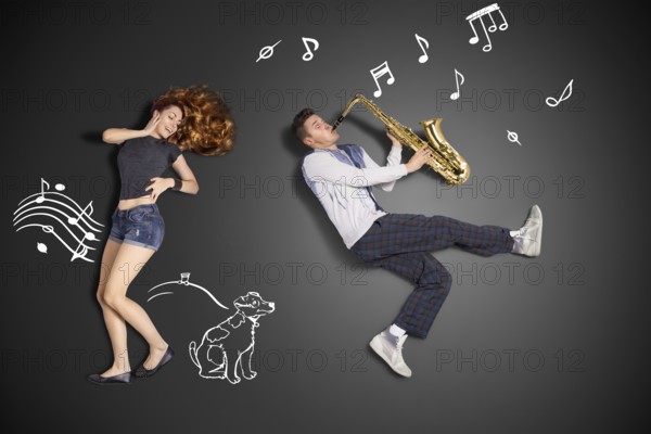 Happy valentines love story concept of a romantic couple against chalk drawings background. Male playing the saxophone for his girlfriend