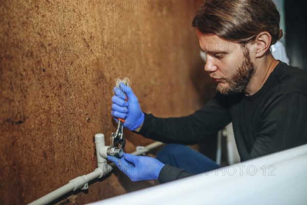 Person using a wrench on a pipe connection while wearing gloves