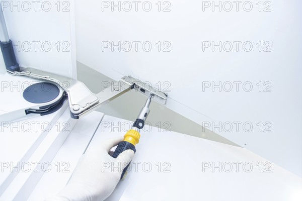 Close-up of a gloved hand fixing a cabinet hinge with a screwdriver