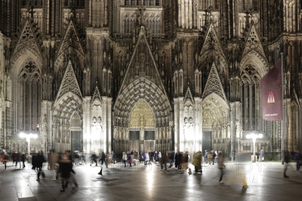 Night view of the cathedral façade with people passing by in the foreground, Domplatte, Roncalliplatz, Cologne, North Rhine-Westphalia, Germany, Europe