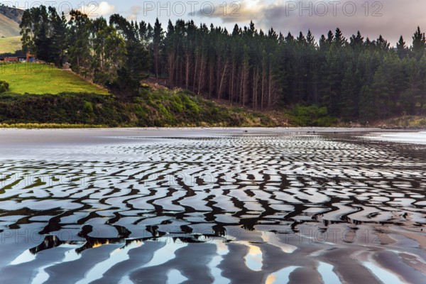Sunrise over the ocean. Low tide. Strips of sand and water left by the ocean tide. The art of artistic photography. New Zealand, Pacific Coast. The concept of artistic photography. Artistic postal card