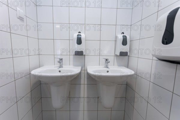 A clean and contemporary public restroom that features two modern washbasins along with convenient hand sanitizers