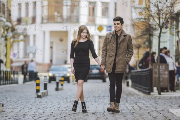 Urban modern young love couple walking romantic talking talking, holding hands on a date. Young multicultural Turkish brunette and Caucasian couple on old european street. Autumn spring weather