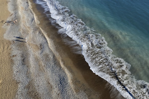 Aerial drone point of view of person walking on sand in a beach. Stormy waves idyllic beach in winter