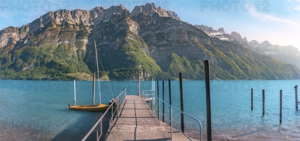 Spring landscape with a pier on the Walensee lake leading toward the Alps mountains, in Switzerland, on a sunny day of spring