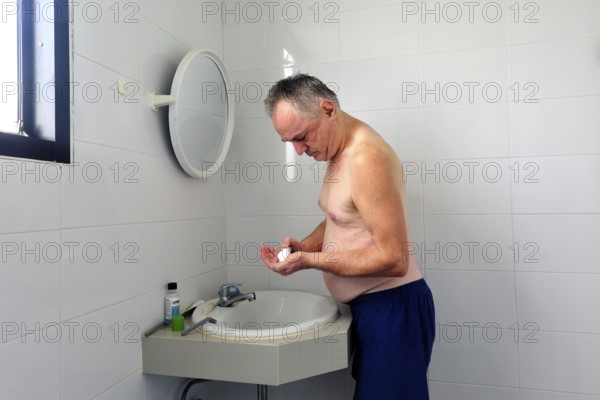 Man 60 plus shaves wet in the bathroom