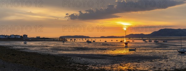 Colorful sunrise on the Menai Strait and mountains of Snowdonia at low tide with Beaumaris village in silhouette
