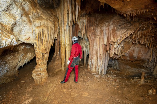 A speleologist with helmet and headlamp exploring a cave with rich stalactite and stalagmite formations. graphy