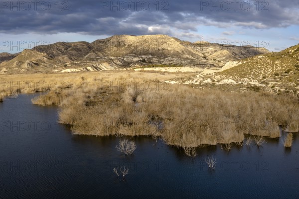 View of a dark blue lake with dry yellow brush and semi-desert mountain and hill landscape behind