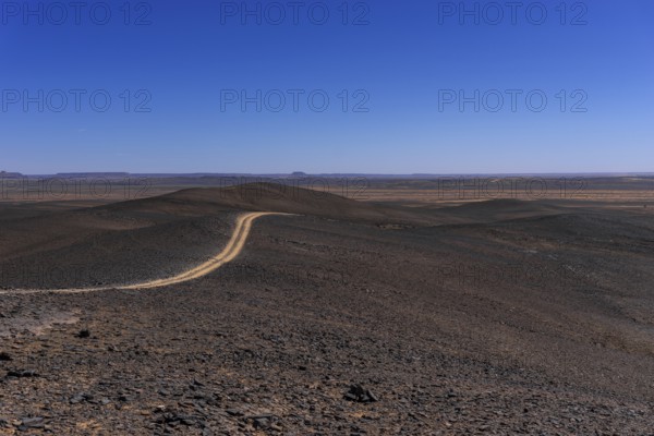 A view of a dirt road leading through the rock and sand desert of southeastern Morocco mear Merzouga and Erg Chebbi
